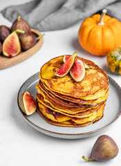 Stack of pumpkin pancakes with honey and figs in a plate on light background with fresh fruits and vegetables.