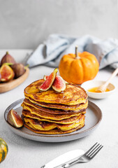 Stack of pumpkin and pancakes with honey and figs on a light background with fresh fruits.