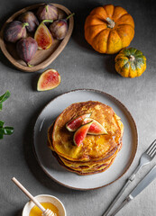 Stack of pumpkin and pancakes with honey and figs on a dark background with fresh fruits and vegetables.