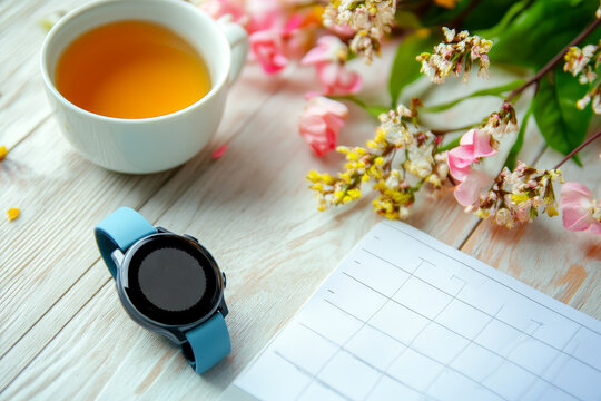 Desk setup with a calendar, tea cup, coffee cup, and greenery in a bright workspace