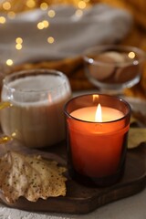 Burning candle, cocoa and dry leaves on table, closeup. Autumn atmosphere