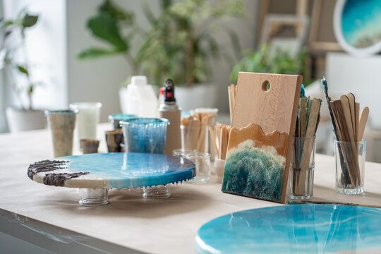 Workplace equipped for working with epoxy resin. Wooden boards, stirring sticks, canvases with drying finished artworks tools for creative process. Necessary supplies for creative process at workspace
