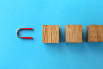 Magnet attracting wooden cubes on light blue background, flat lay