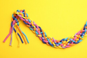Braided colorful ropes on yellow background, top view. Unity concept