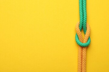 Colorful ropes tied in knot on yellow background, top view with space for text. Unity concept