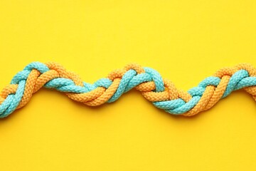 Colorful ropes tied together on yellow background, top view. Unity concept