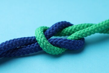 Colorful ropes tied in knot on light blue background, closeup. Unity concept