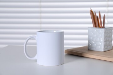 One blank ceramic mug and stationery on white table. Mockup for design