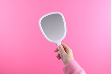 Woman holding handheld mirror on pink background, closeup © New Africa