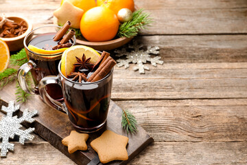 Tasty mulled wine with spices, orange slices, cookies and Christmas decor on wooden table. Space for text