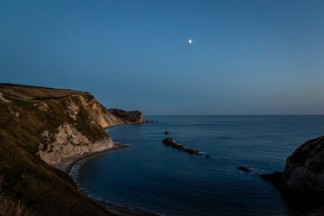 Man o war beach after sunset, Image shows the beach next to Durdle door after sunset with a calm bay and visible moon