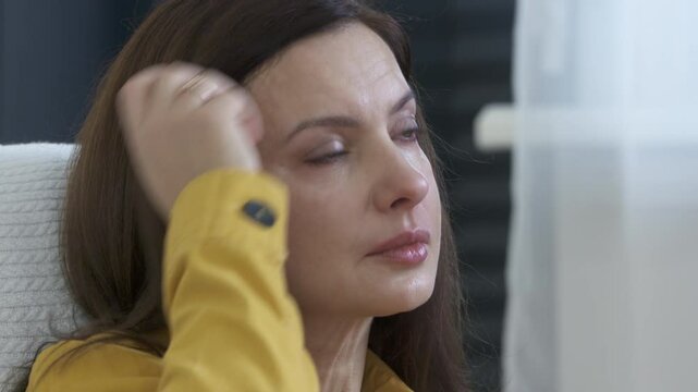 Adult 44 year old woman sitting on sofa in living room in front of TV watching melodrama. Impressionable woman cries wiping tears worried while watching movie.