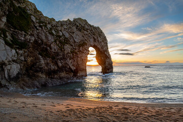 Durdle door at sunset, Image shows the famous arch photographed from the beach with the setting sun seen through the arch