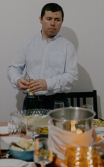 A young man opens a bottle of champagne at the table.