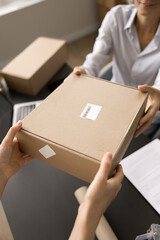 Internet shop storage worker giving cardboard box to female customer over workplace table. Client...