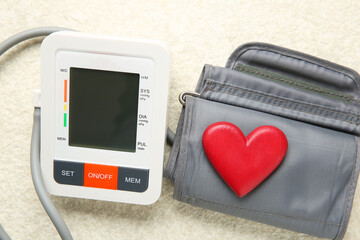 Blood pressure measuring device and heart figure on light textured background, closeup