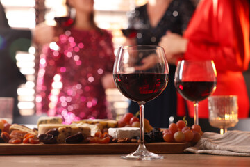 People holding glasses of wine at party, focus on wooden table with snacks and alcohol