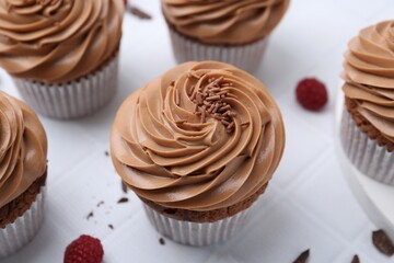Tasty cupcakes with chocolate cream and raspberries on white tiled table, closeup
