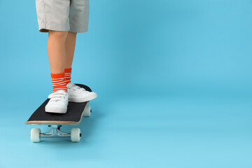 Little boy with skateboard on light blue background, closeup. Space for text
