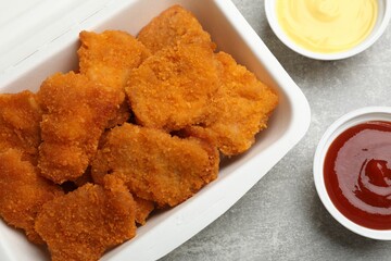 Delicious chicken nuggets in takeaway container with sauces on grey textured table, flat lay