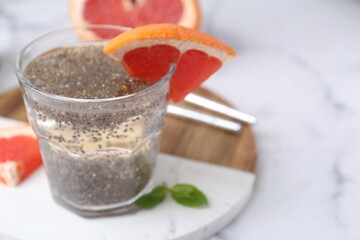 Glass of drink with chia seeds and grapefruit on white marble table, closeup. Space for text