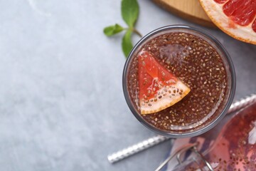 Glass of drink with chia seeds and grapefruit on grey table, flat lay. Space for text