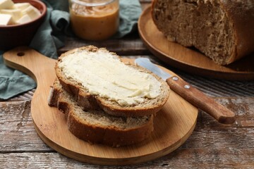 Fresh bread with butter and knife on wooden table, closeup