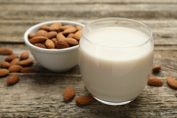 Fresh almond milk in glass and nuts on wooden table, closeup