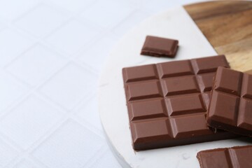 Pieces of delicious milk chocolate on white tiled table, closeup. Space for text