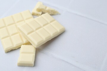 Pieces of delicious white chocolate on tiled table, closeup. Space for text