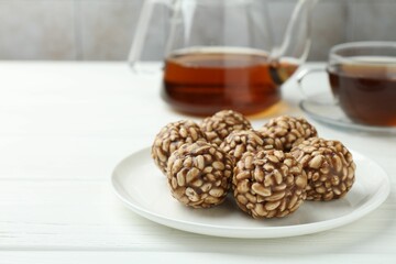 Tasty chocolate puffed rice balls and tea on white wooden table, closeup. Space for text