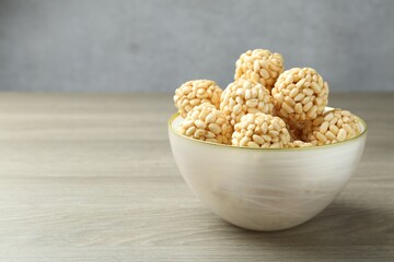Tasty puffed rice balls in bowl on wooden table, closeup. Space for text