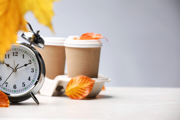 Alarm clock, dry leaves and cups of coffee on light grey background, closeup. Space for text
