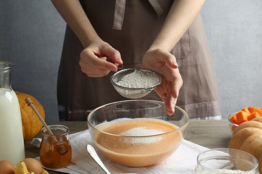 Making pumpkin pancakes. Woman adding flour to dough at table, closeup