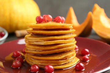 Tasty pumpkin pancakes with cranberries and honey on plate, closeup