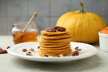 Tasty pumpkin pancakes with nuts and honey on light grey table, closeup