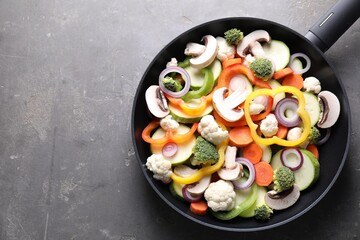 Frying pan with mix of vegetables and mushrooms on grey table, top view. Space for text