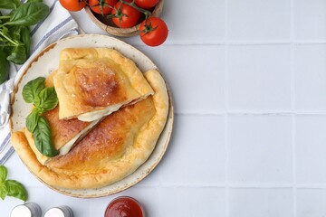 Pieces of delicious calzone pizza with mozzarella, tomatoes and basil on white tiled table, flat lay. Space for text