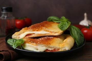 Pieces of delicious calzone pizza with mozzarella, tomatoes and basil on wooden table, closeup