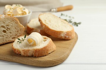 Cut baguette with butter and herbs on white wooden table, closeup