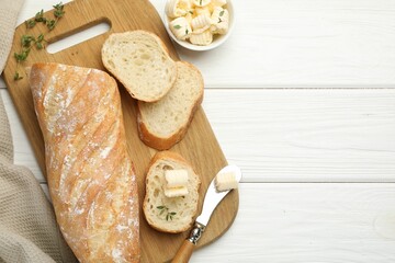 Cut baguette with butter and herbs on white wooden table, flat lay. Space for text