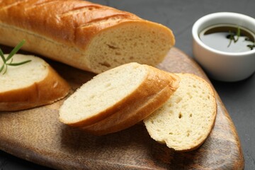 Cut fresh baguette with balsamic and rosemary on black table, closeup