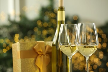 Glasses and bottle of white wine against blurred Christmas lights, closeup. Bokeh effect