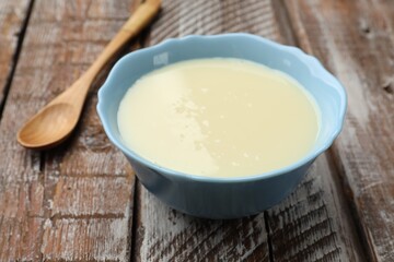 Condensed milk in bowl and spoon on wooden table, closeup
