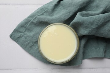 Tasty condensed milk in bowl and towel on white tiled table, top view