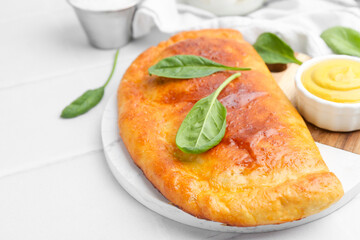 Tasty calzone with basil and sauce on white table, closeup. Space for text