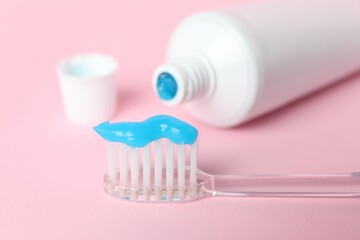 Toothbrush with toothpaste and tube on pink background, closeup