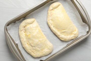 Uncooked calzone pizza in baking dish on white wooden table, top view