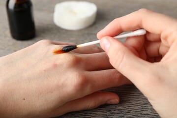 Woman applying topical iodine with cotton swab on hand at wooden table, closeup