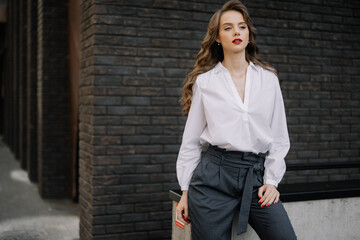 Businesswoman leaning against wall wearing white shirt and grey pants